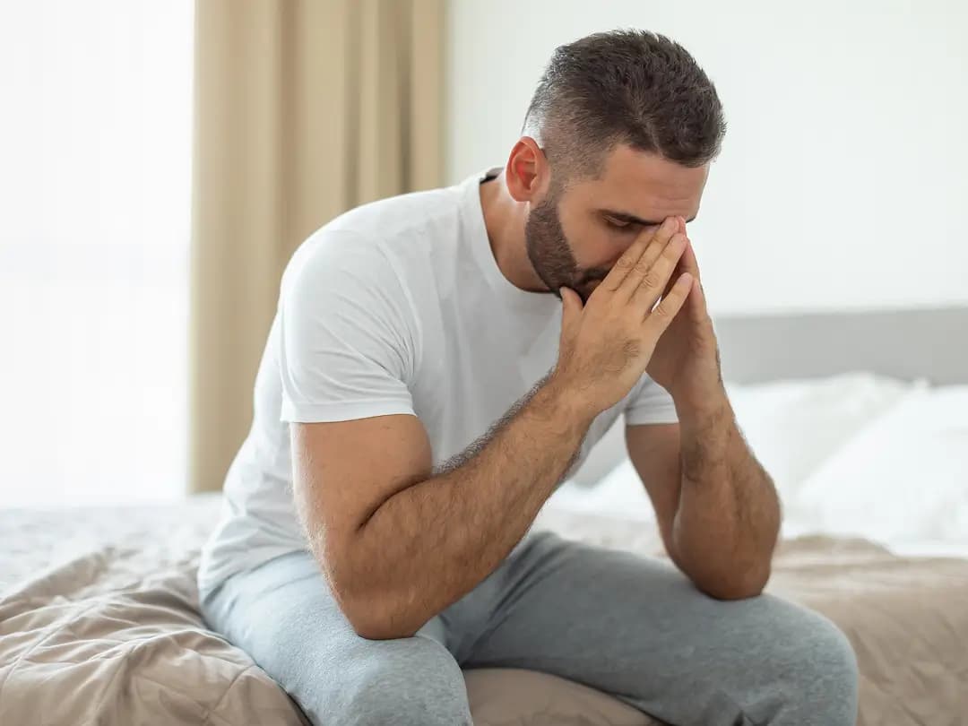 A man sitting on the edge of a bed with his head in his hands